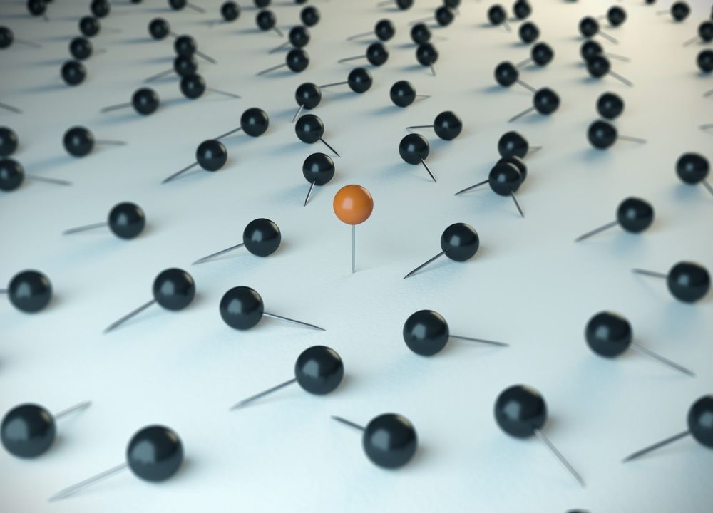 A single orange pin standing out among many black pins